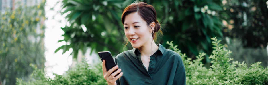 woman smiling while looking at her phone in a green area